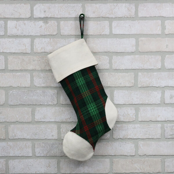 A green and black Tartan Stocking with Toes - Homespun Wool Blend hanging on a brick wall.