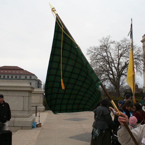 A Medium Ancient Kid Kilt, including kids, proudly holding a flag in front of a building.