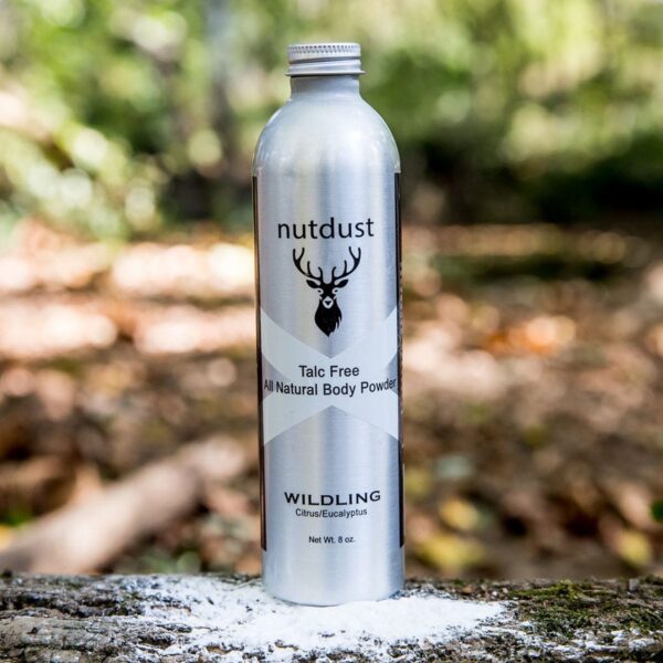 A bottle of Nutdust -Wildling body powder sits on top of a tree, surrounded by Wildling foliage.