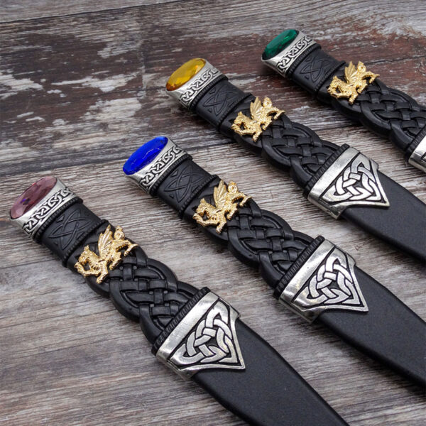 A set of four black and gold knives, including the traditional Scottish Sgian Dubh, displayed elegantly on a polished wooden surface.