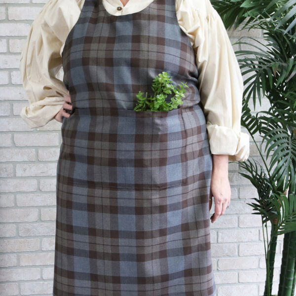 A woman wearing a Tartan Cross Back Apron - Homespun Wool Blend with a plant in it.