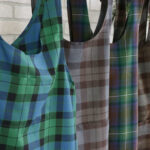 Four Tartan Cross Back Aprons - Homespun Wool Blend hanging on a rack.