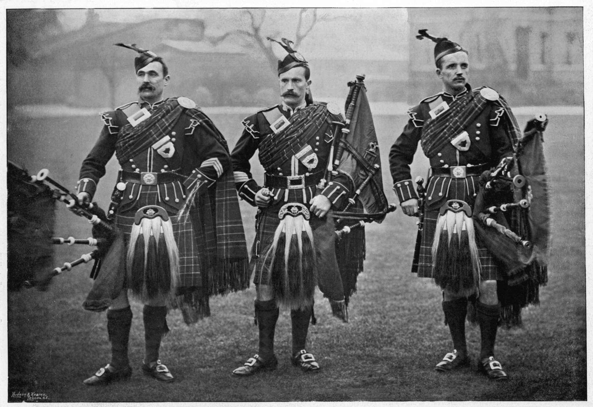 Three men in a black and white historical photo wearing sporrans and bagpipes.