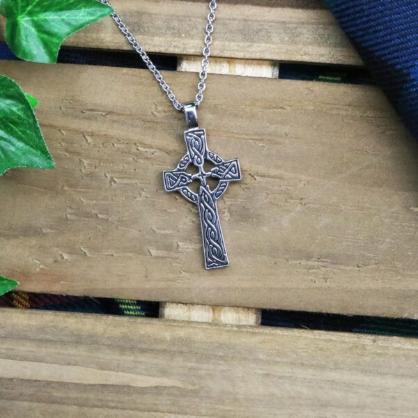 A silver celtic cross necklace on a wooden table.