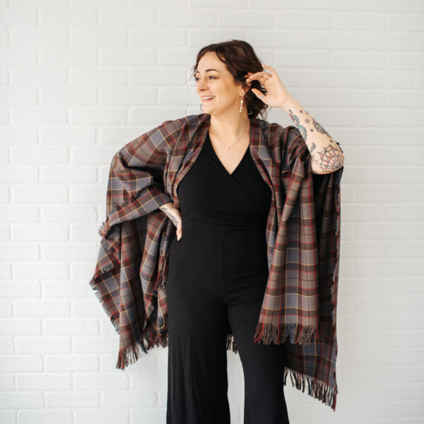 A woman wearing a black jumpsuit and an OUTLANDER Wrap Premium Lambswool Tartan.