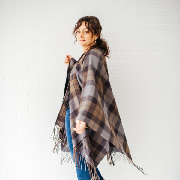 A woman wearing an OUTLANDER Wrap Premium Lambswool Tartan standing in front of a white wall.