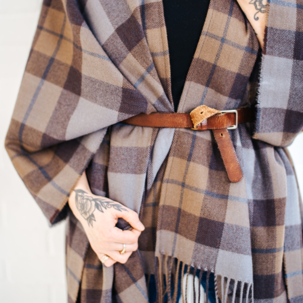 A woman wearing an OUTLANDER Wrap Premium Lambswool Tartan poncho with a belt.