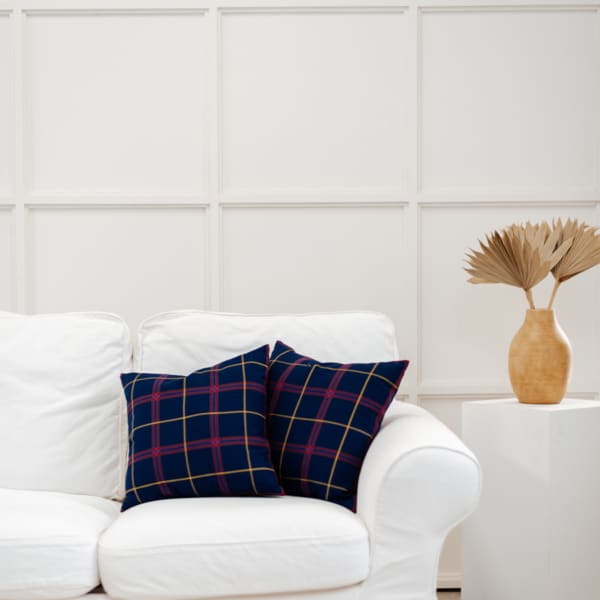 A white couch with plaid pillows and a vase.