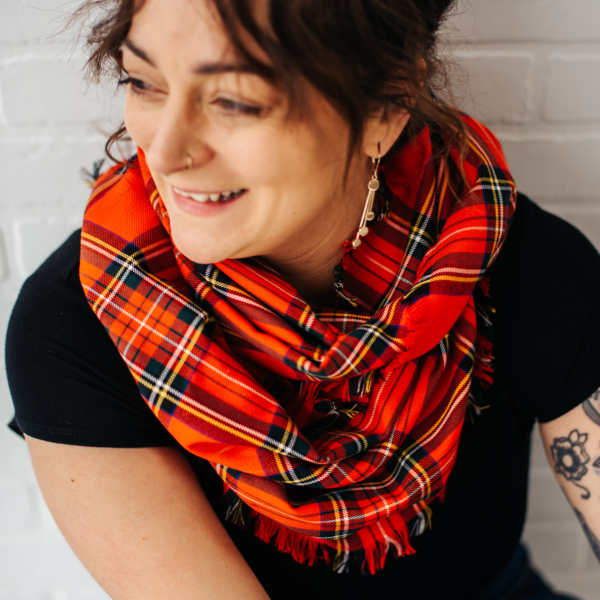A woman with tattoos wearing a red Tartan Scarf - 13oz Premium Wool, adorned with a medium weight.