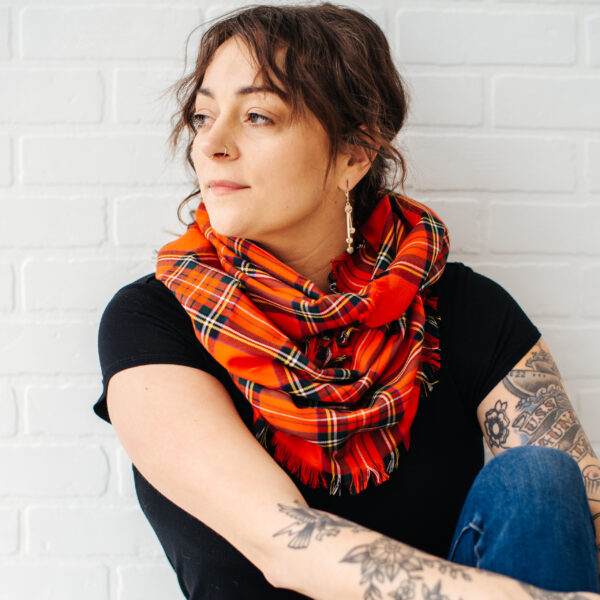 A woman with tattoos wearing a Tartan Infinity Scarf - Poly/Viscose Wool Free.