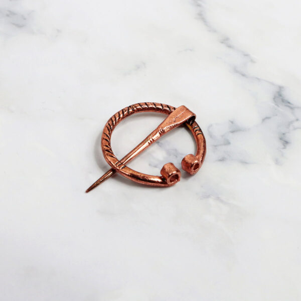 A mini rose gold Mini Penannular Brooch on a marble table.